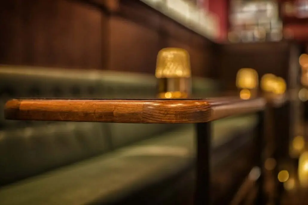 Detalj av trelist og grønn sittebenk på O'Learys Drammen, med tente bordlamper i bakgrunnen.