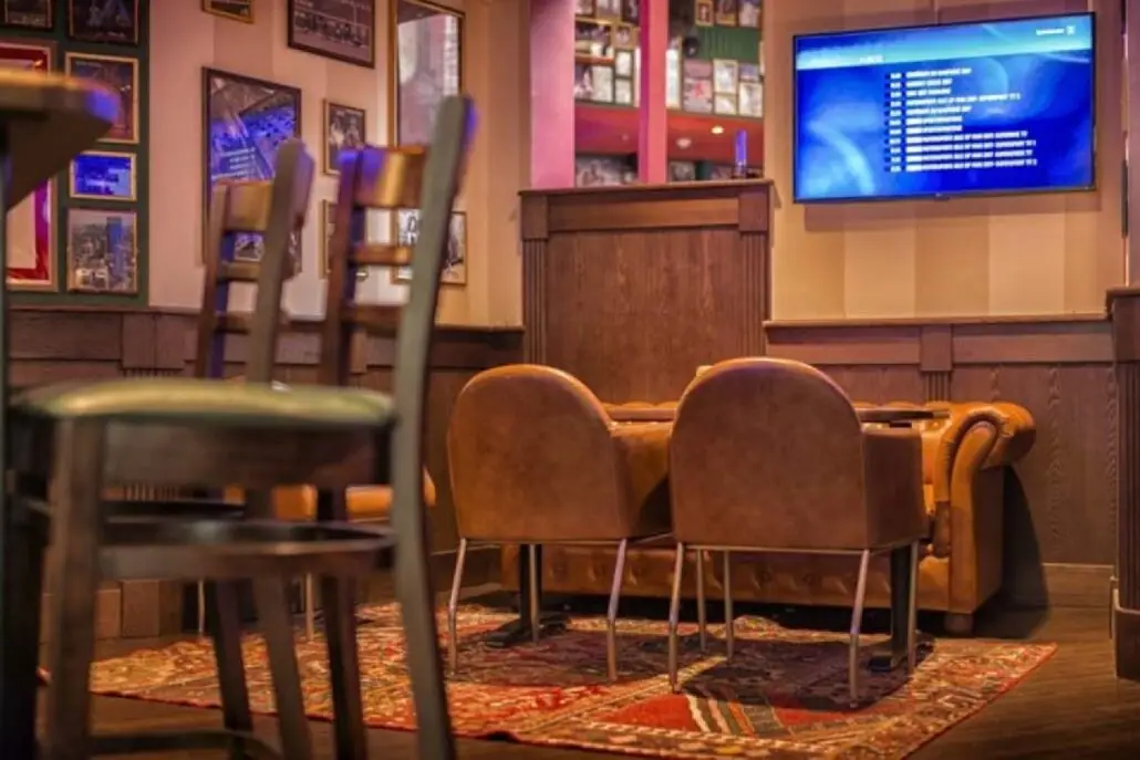 Loungeområde på O'Learys Drammen med skinnsofa, lenestoler og TV-skjerm på veggen.