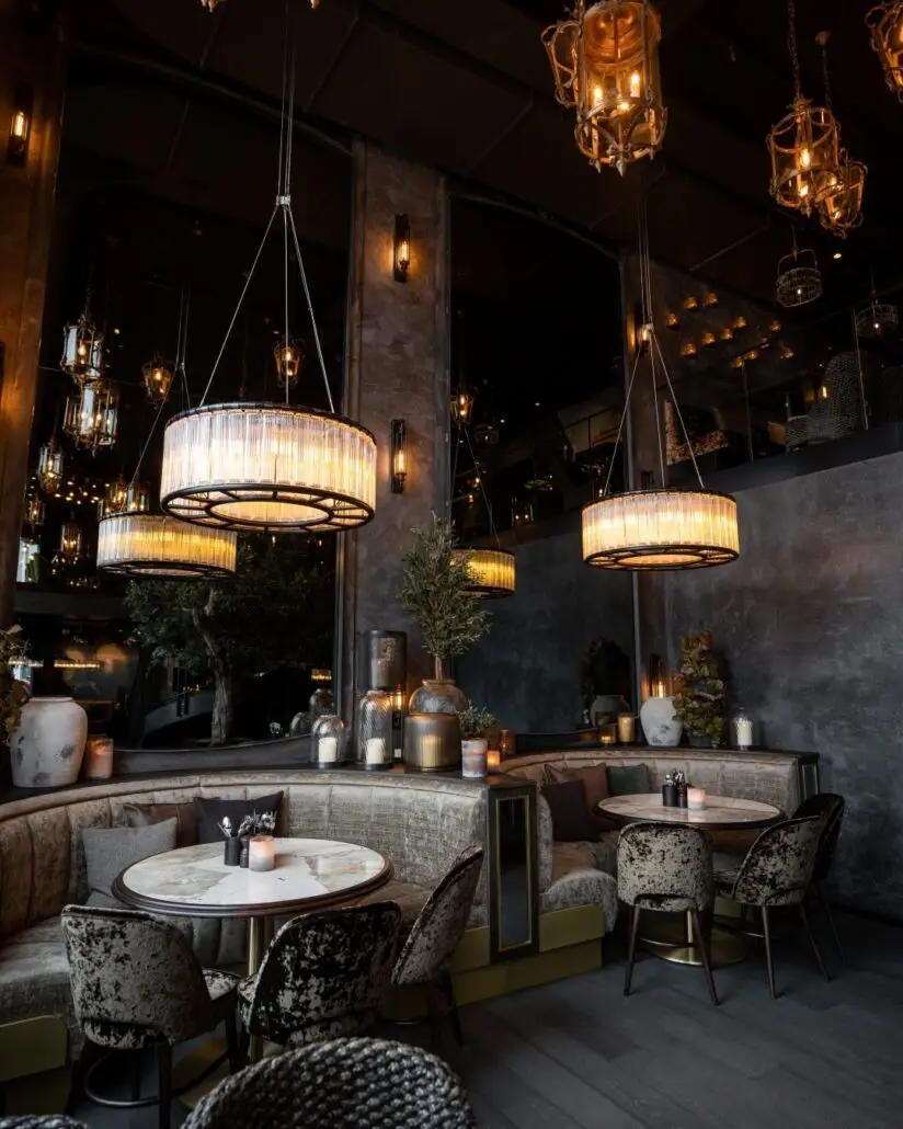 Restaurantinteriør på Olivia Vågen med runde marmorbord, velurseter og store hengelamper som skaper en stemningsfull atmosfære.