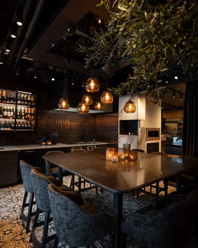 Stemningsfullt interiør på Olivia Ramsalt med høyt marmorbord, velurstoler, hengelamper og vinbar i bakgrunnen.
